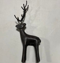 Load image into Gallery viewer, The Cast Iron Deer, a small dark sculpture with prominent antlers, stands on a light surface casting a gentle shadow—a charming decorative accent for rustic home décor.