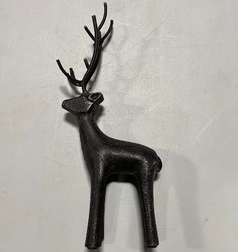 The Cast Iron Deer, a small dark sculpture with prominent antlers, stands on a light surface casting a gentle shadow—a charming decorative accent for rustic home décor.