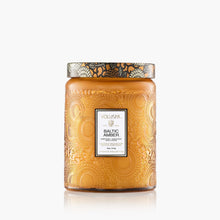 Load image into Gallery viewer, The Voluspa 18oz Glass Jar Candle features amber-colored embossed glass with floral patterns and a metallic lid, labeled "Voluspa Baltic Amber." Made from coconut wax, the candle is displayed against a white background.