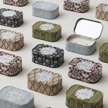 Load image into Gallery viewer, Several Cherie Tin 4.5 oz Candles featuring floral and geometric designs are arranged neatly on a light surface, with one tin open to reveal a lit double-wick decorative scented candle inside.