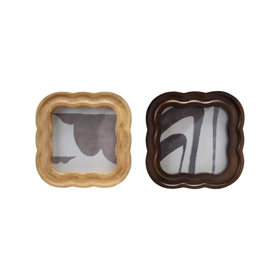 Two Scalloped Square Frame trays—one with a light rubberwood frame and abstract black-gray shapes, the other in dark wood with bold black-and-white accents—are shown from above on a white background.