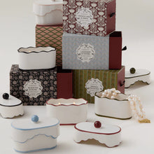 Load image into Gallery viewer, The 5.5oz Ceramic Dish Candle by Paddywax in white lidded containers is displayed with boxes labeled lavender, thyme, and black fig; a pearl necklace rests nearby.