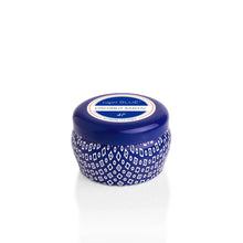 Load image into Gallery viewer, A Capri Blue Mini Tin candle in a small blue jar with a white patterned design and round lid, labeled Coconut Santal and reminiscent of the Volcano scent, is displayed on a white background.