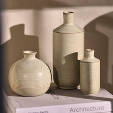 Load image into Gallery viewer, A Minty Green Cove Budvase sits atop a closed book titled Architecture, its unique ceramic shape highlighted by soft sunlight that casts gentle shadows on the wall behind it.