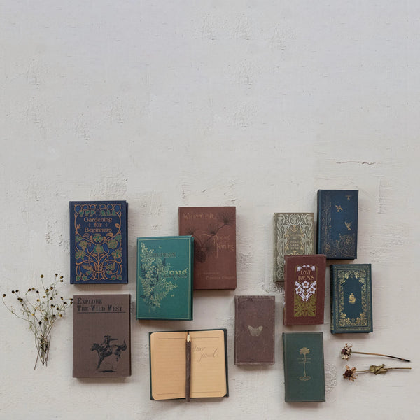 A set of Canvas Journals in 4 styles, some open and some closed, are arranged on a light textured surface with dried flowers scattered nearby.