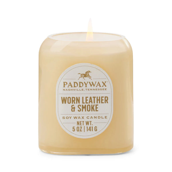 A lit 5oz Vista Candle in "Worn Leather & Smoke" scent fills the room with a luxurious aroma. The simple glass jar label shows the brand, fragrance, 5 oz (141 g) weight, and Nashville, Tennessee origin.