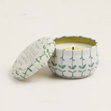 Load image into Gallery viewer, The Printed Tulip Candle Tin, featuring a white gardenia scent, sits lit in its round tin adorned with green leaf and bamboo patterns. The matching lid is set aside as the fresh, floral aroma fills the light-colored background.