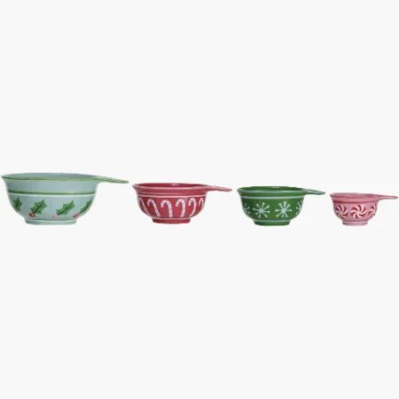 The Christmas Stoneware Measuring Cups set includes four handled cups with festive holly, candy cane, snowflake, and peppermint swirl designs—perfect for holiday baking.