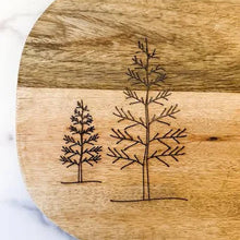 Load image into Gallery viewer, The Mango Wood Tree Cutting Board is handcrafted from mango wood and features two hand-etched pine trees, highlighting the natural grain for a charming charcuterie or serving board for any occasion.