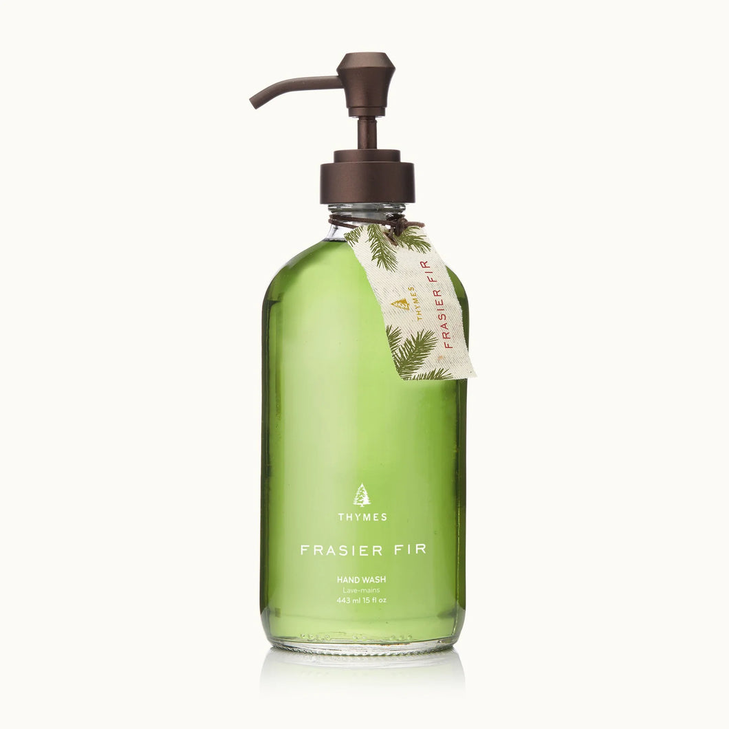 A clear glass pump bottle from the Frasier Fir Home Care Collection holds green hand wash and features a pine-decorated tan tag—a signature winter fragrance for your home.