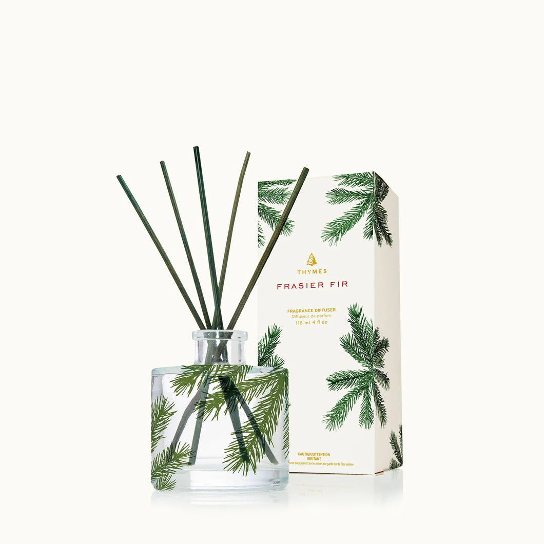 The Frasier Fir Heritage Collection features a clear glass diffuser with green reeds and pine needle accents, paired with a matching box adorned with pine branch designs on white for a fresh evergreen ambiance.
