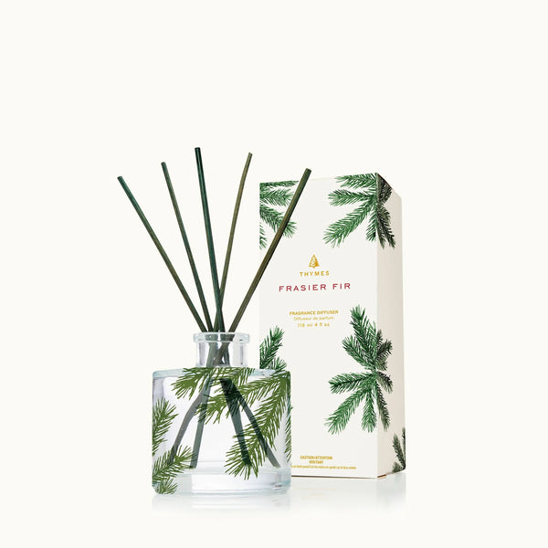 The Frasier Fir Heritage Collection features a clear glass diffuser with green reeds and pine needle accents, paired with a matching box adorned with pine branch designs on white for a fresh evergreen ambiance.