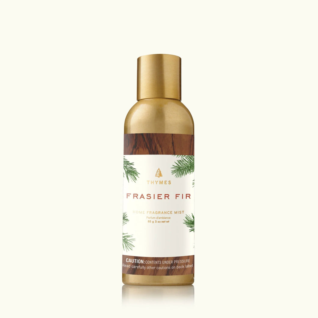 An upright gold and bronze Thymes Frasier Fir Home Care Collection fragrance mist can features pine branch artwork, offering a touch of winter to any room.