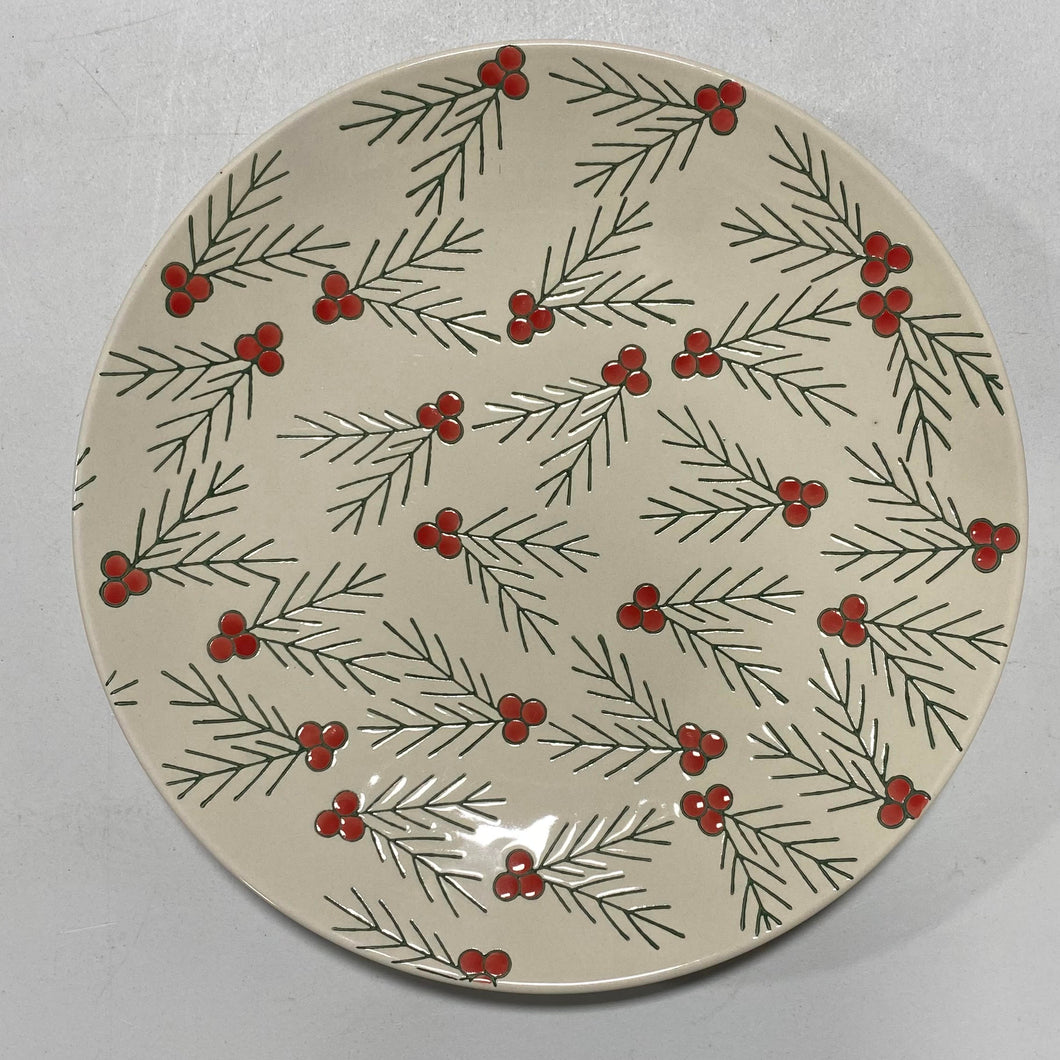 The Hand Painted Floral Holly Plate is a round handcrafted stoneware plate with a cream background, adorned with green pine branches and bright red berry clusters.