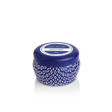 Load image into Gallery viewer, A small, round blue Capri Blue Mini Tin candle with a patterned design and matching lid features a label reading “capri BLUE VOLCANO.” The candle stands out against the plain white background.
