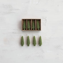 Load image into Gallery viewer, Four green, unscented pine tree-shaped candles from the Box/4 Shaped Candles set sit in a brown box, with one displayed outside—all shown on a textured white surface, ideal for holiday décor.