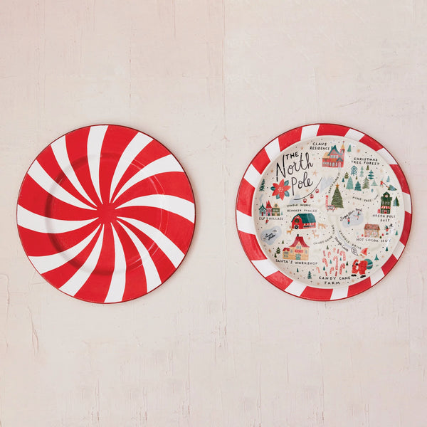 Two round plates on a light surface: the left has red and white peppermint swirls, while the right is the North Pole Plate featuring colorful holiday stoneware illustrations and seasonal designs.